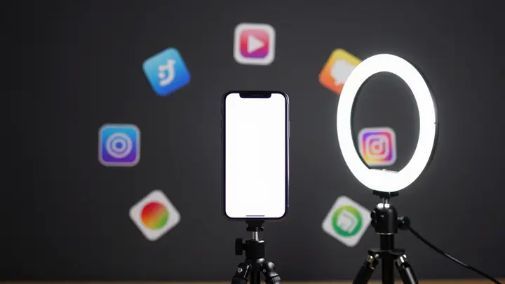 Minimalist flat lay of a smartphone on a tripod with ring light, surrounded by social media icons and app icons, dark ba