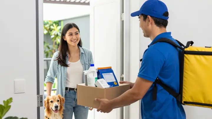 Bright photo of a delivery courier handing a box of pet food and supplies to a happy pet owner at their apartment door, 