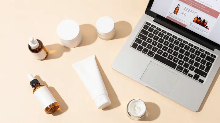 Flat lay of skincare and beauty products on a clean pastel background with a laptop showing an online store, soft natura