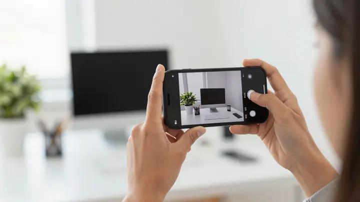 A person holding a smartphone taking a photo of a bright modern workspace, stock photography concept, clean composition,